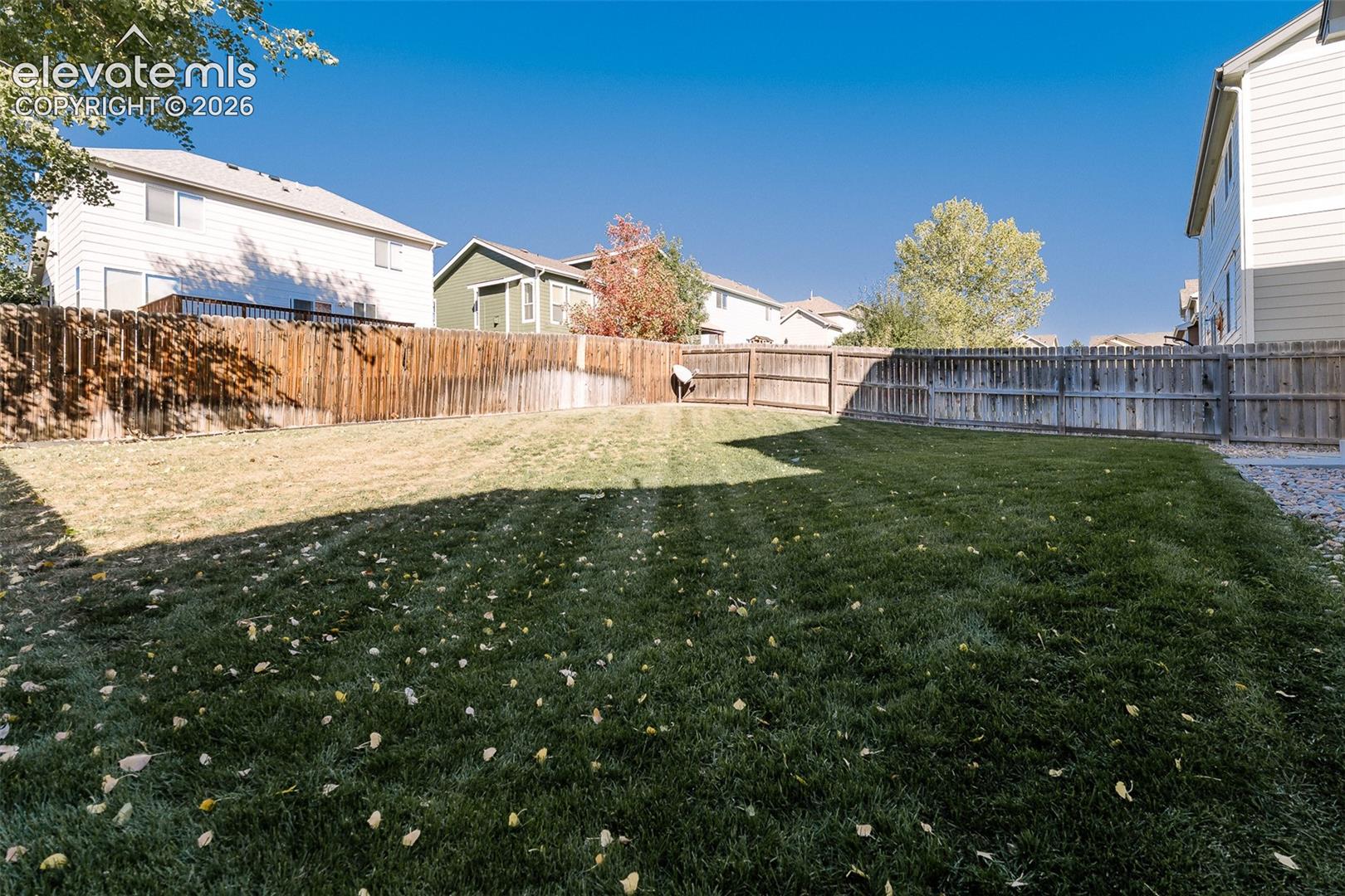 Backyard featuring a grass lawn, perimeter wood fencing, and mature trees