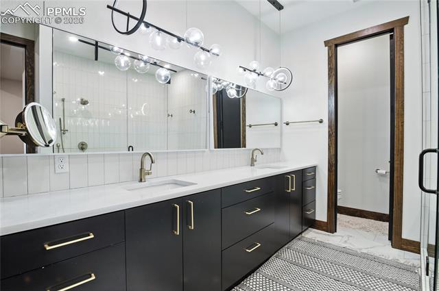 Full bath featuring a stall shower, double vanity, and light marble finish flooring