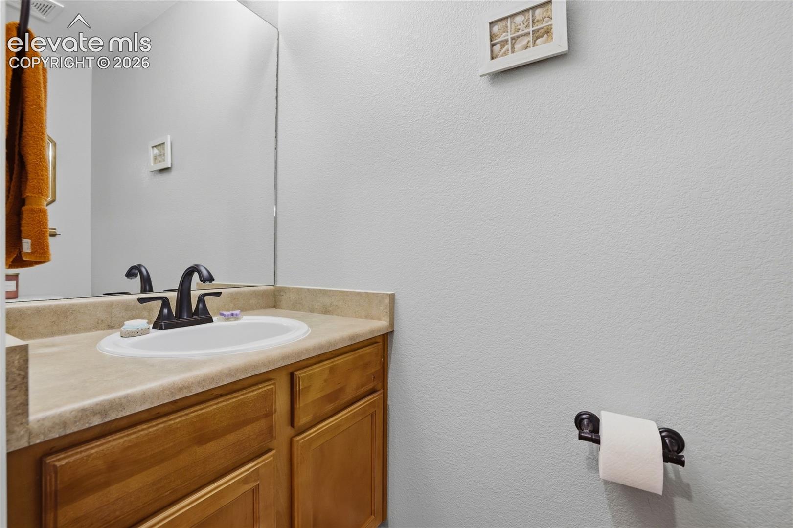 Half-bath with wood-finish vanity with an integrated sink, a neutral countertop, and a dark-finish faucet