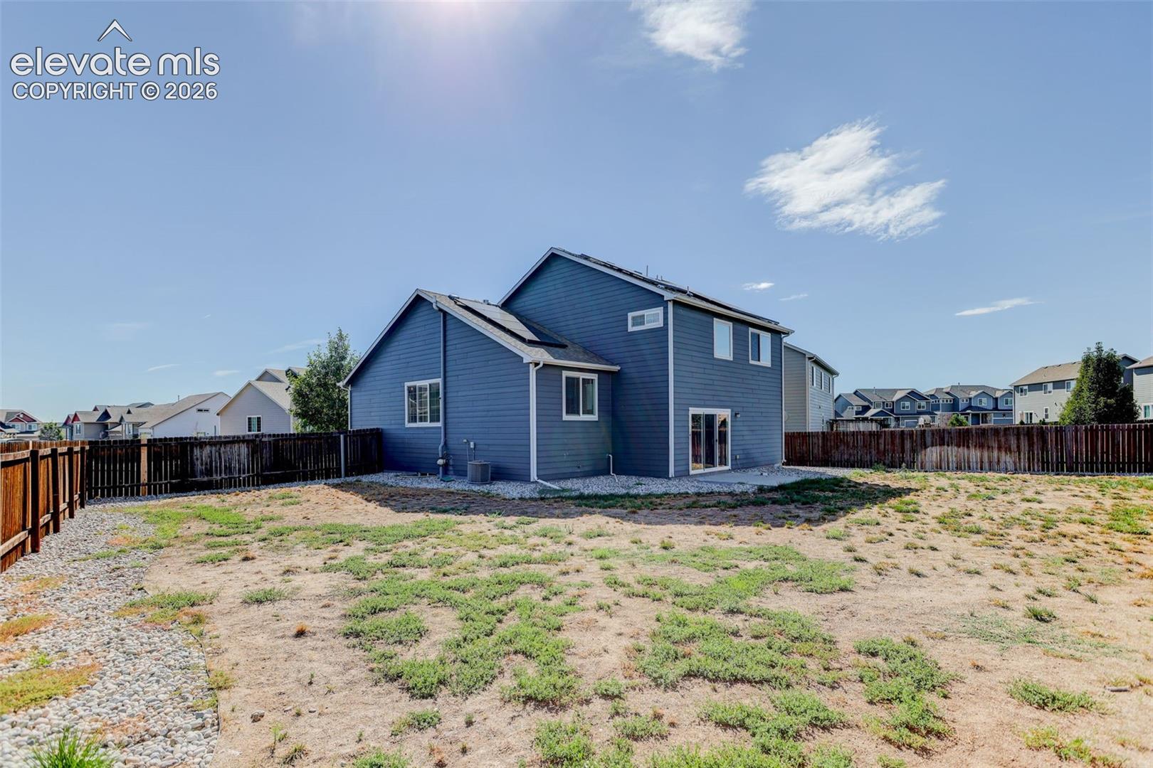 Expansive backyard featuring a partial wood fence, gravel border, and a two-story exterior with blue siding