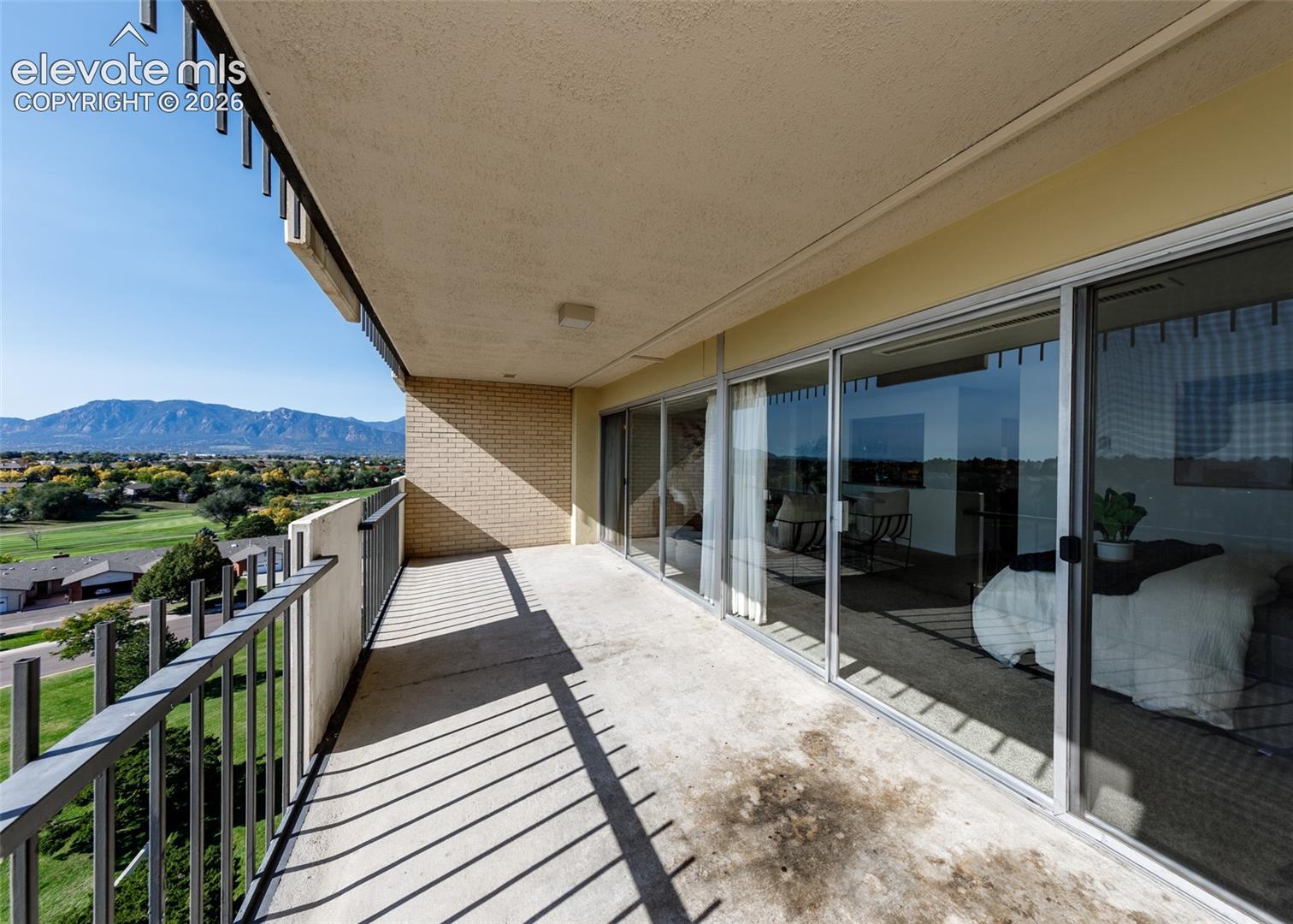 Expansive covered balcony featuring concrete flooring, brick wall detailing, a full-length metal railing, and floor-to-ceiling sliding glass doors