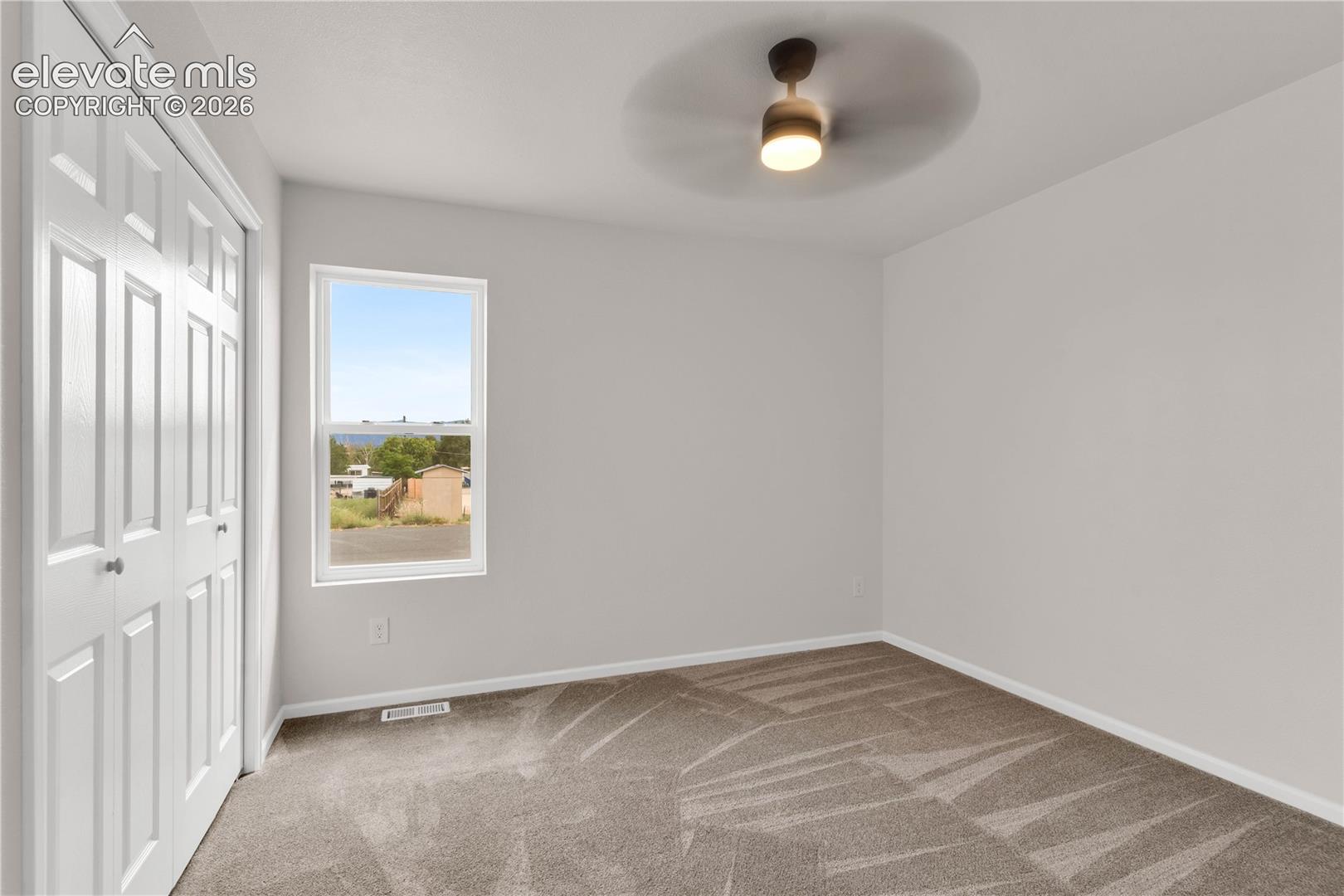 Interior space featuring wall-to-wall carpeting, a multi-panel bi-fold closet door, neutral wall paint, and a ceiling-mounted light fixture with an integrated fan