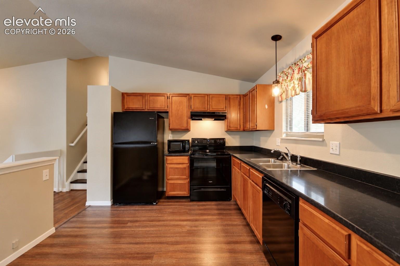 Kitchen featuring wood cabinetry, solid-surface countertops, black appliances, wood-finish flooring, and vaulted ceilings