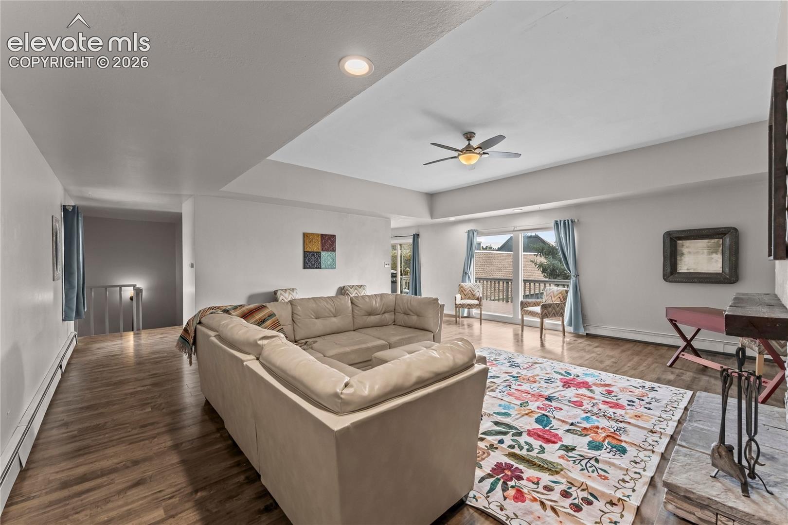 Open-concept room featuring a tray ceiling, recessed lighting, wood-finish flooring, a ceiling fan, and sliding glass doors