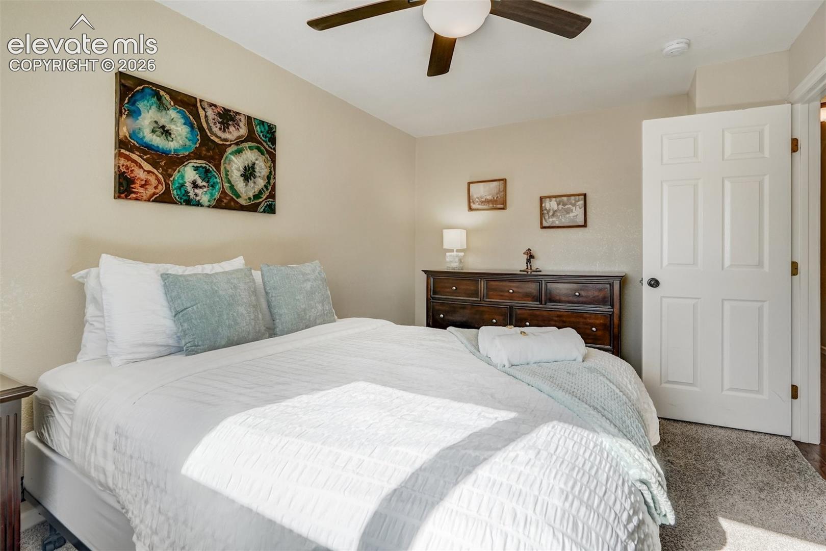 Neutral wall tones complement the ceiling fan with integrated lighting, wood-finish dresser, and paneled interior door