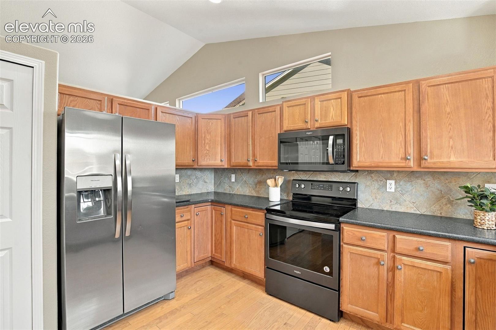 Kitchen featuring stainless steel refrigerator, black range, black microwave, wood-finish cabinetry, and dark countertops