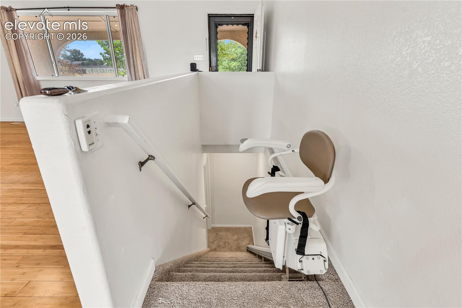 Carpeted staircase with an installed stair lift system, featuring a handrail and textured walls