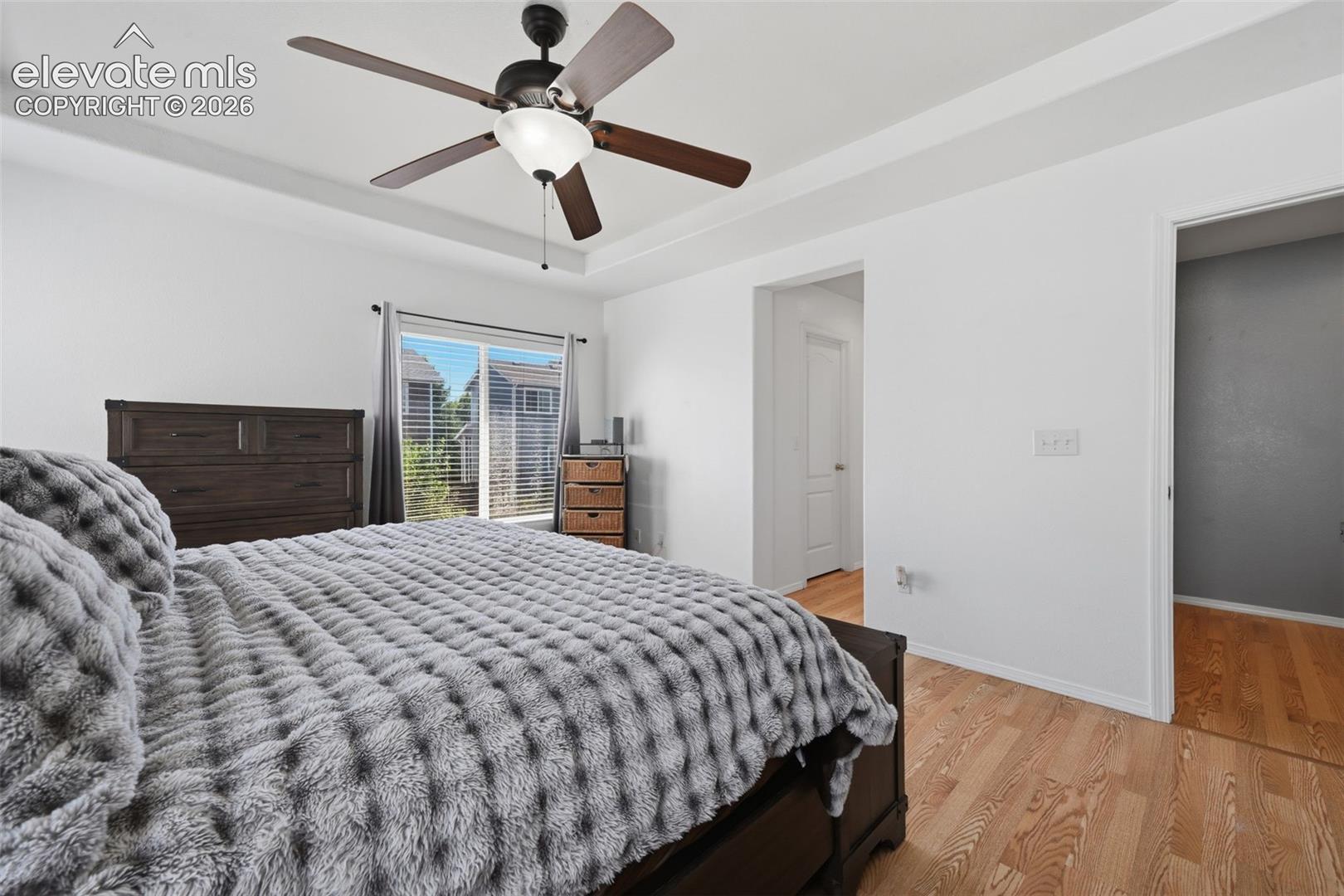 Tray ceiling with a ceiling fan, wood-finish flooring, sliding glass door with blinds, and white interior doors