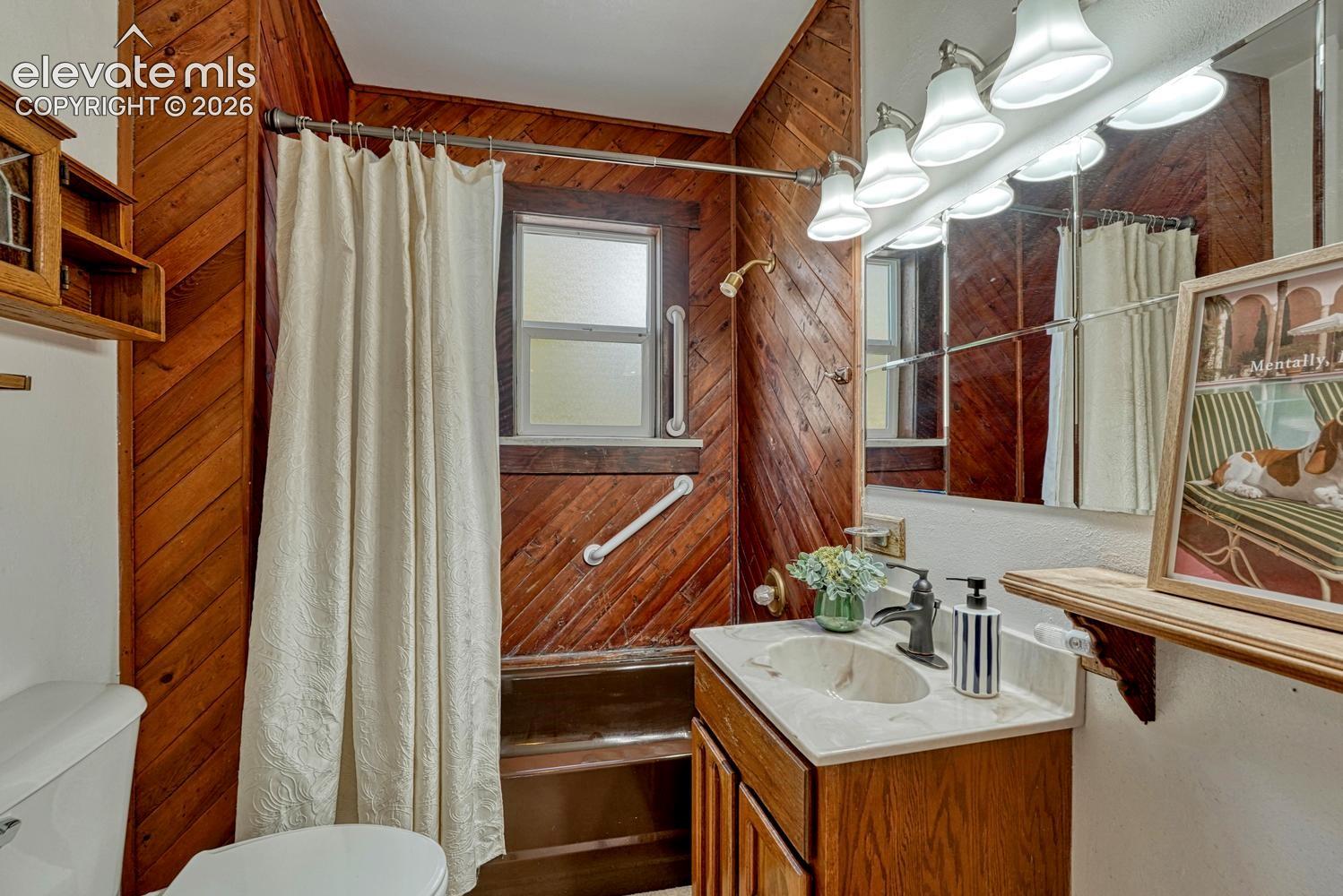 Wood-paneled bathroom featuring a shower with a grab bar, a vanity with a sink, and a large mirror with integrated lighting
