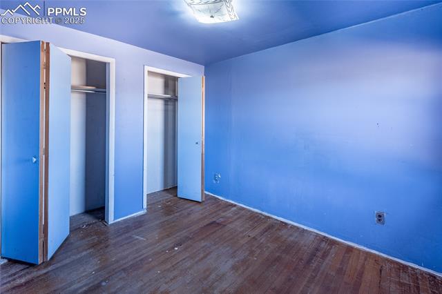 Unfurnished bedroom with two closets and dark wood-type flooring