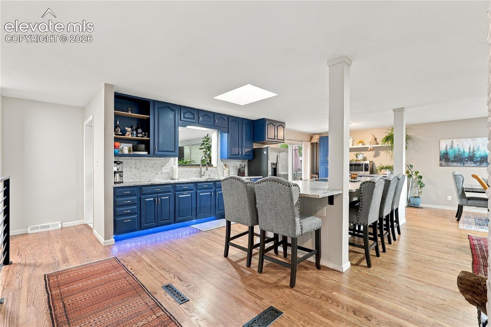 Kitchen featuring blue cabinetry, stone-finish countertops, an integrated breakfast bar, wood-finish flooring, and a ceiling skylight