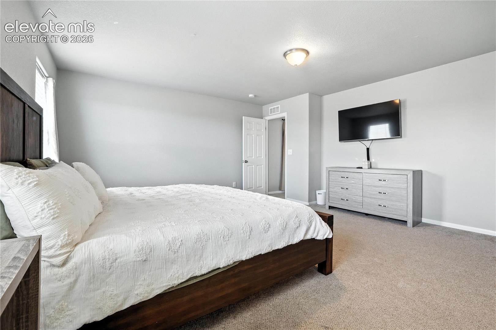 Vaulted ceiling, wall-mounted television, neutral carpeting, flush mount ceiling light fixture, and light gray wall paint