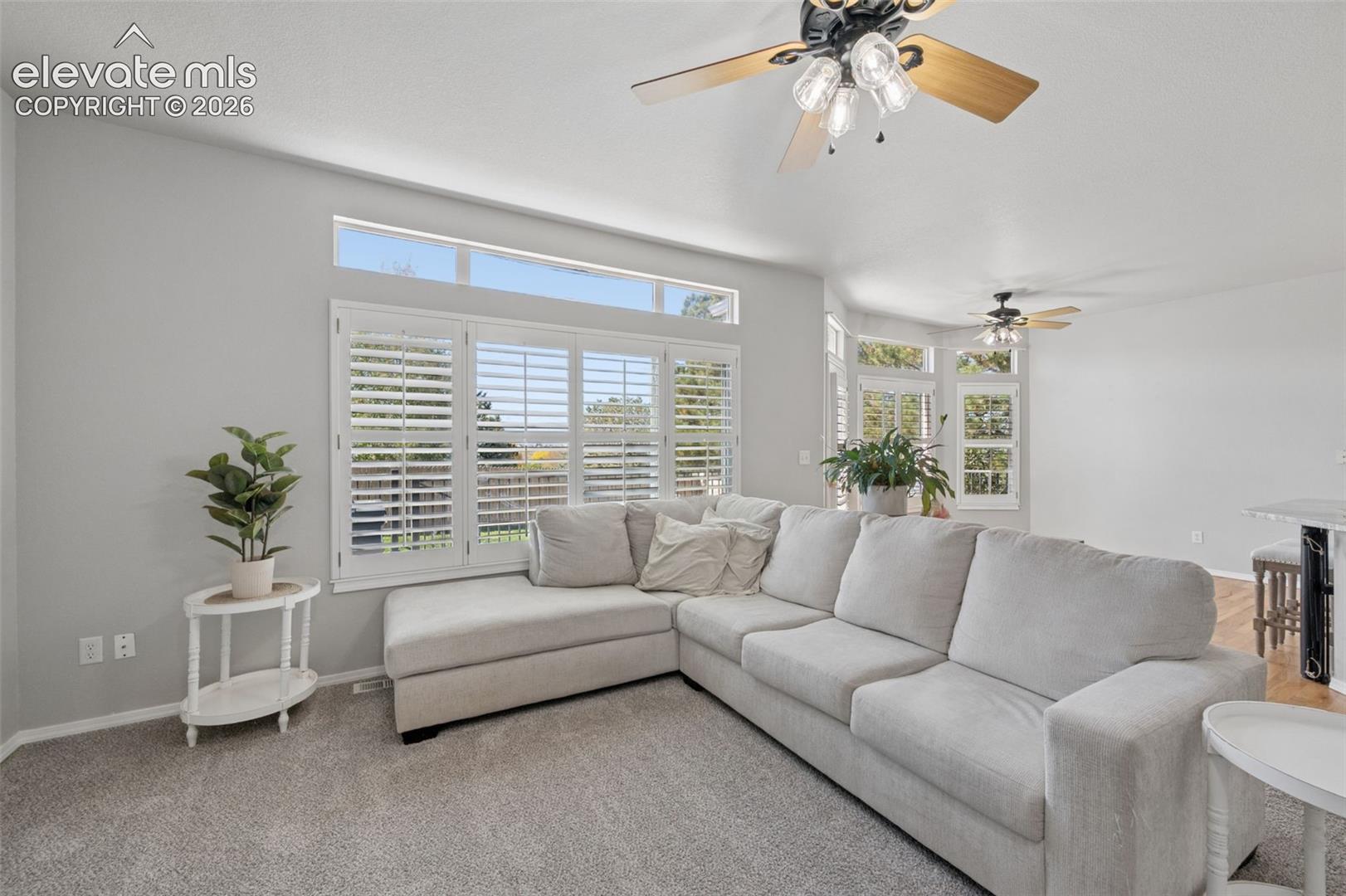 Living area featuring tiered transom windows, plantation shutters, and ceiling fans