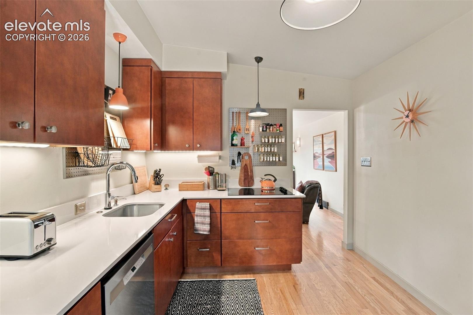 Kitchen featuring flat-panel wood cabinetry, white stone countertops, an undermount stainless steel sink, under-cabinet lighting, and wood flooring