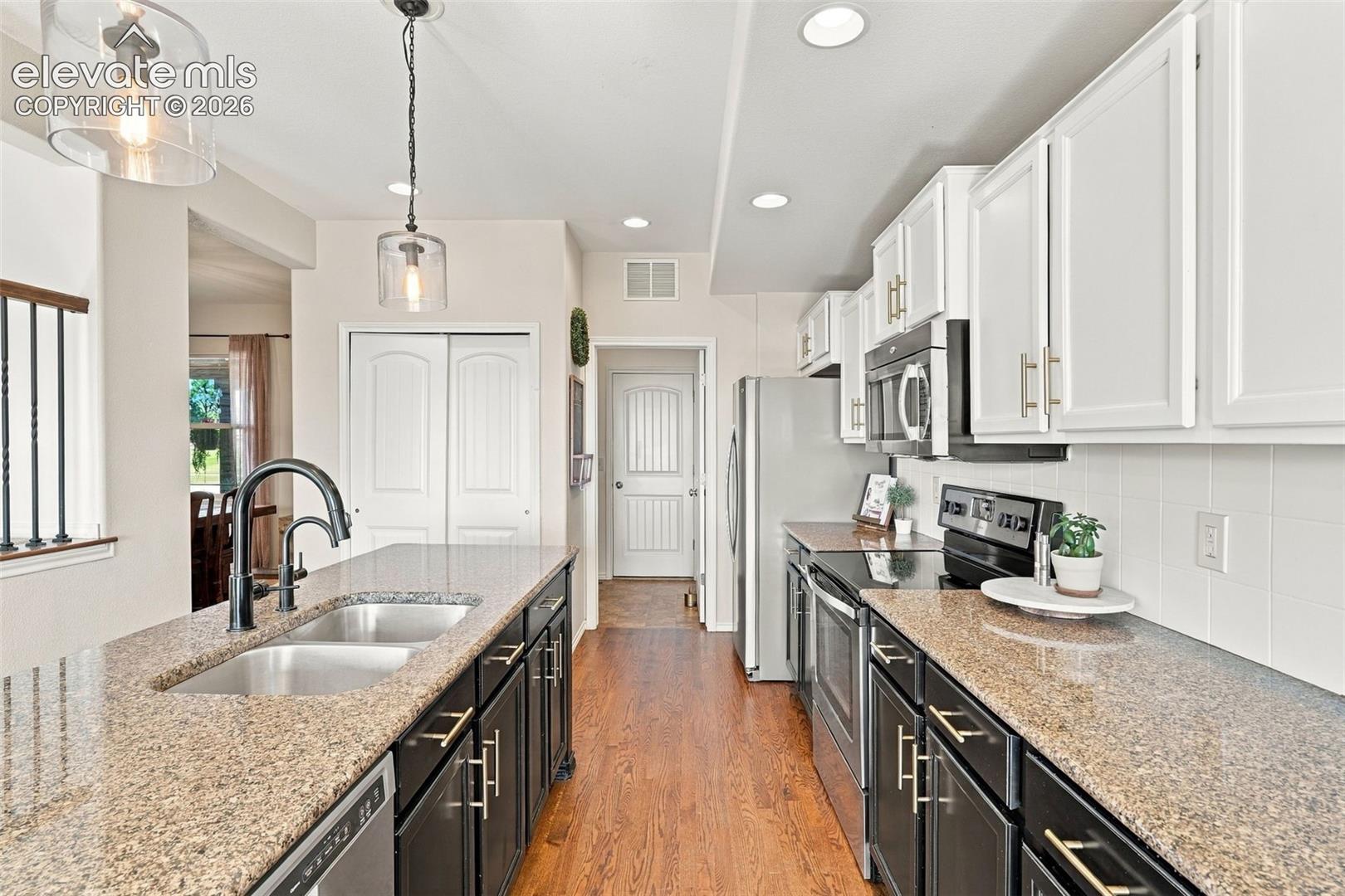 Kitchen featuring stone-finish countertops, dark lower cabinetry, white upper cabinetry, stainless steel appliances, and wood-finish flooring