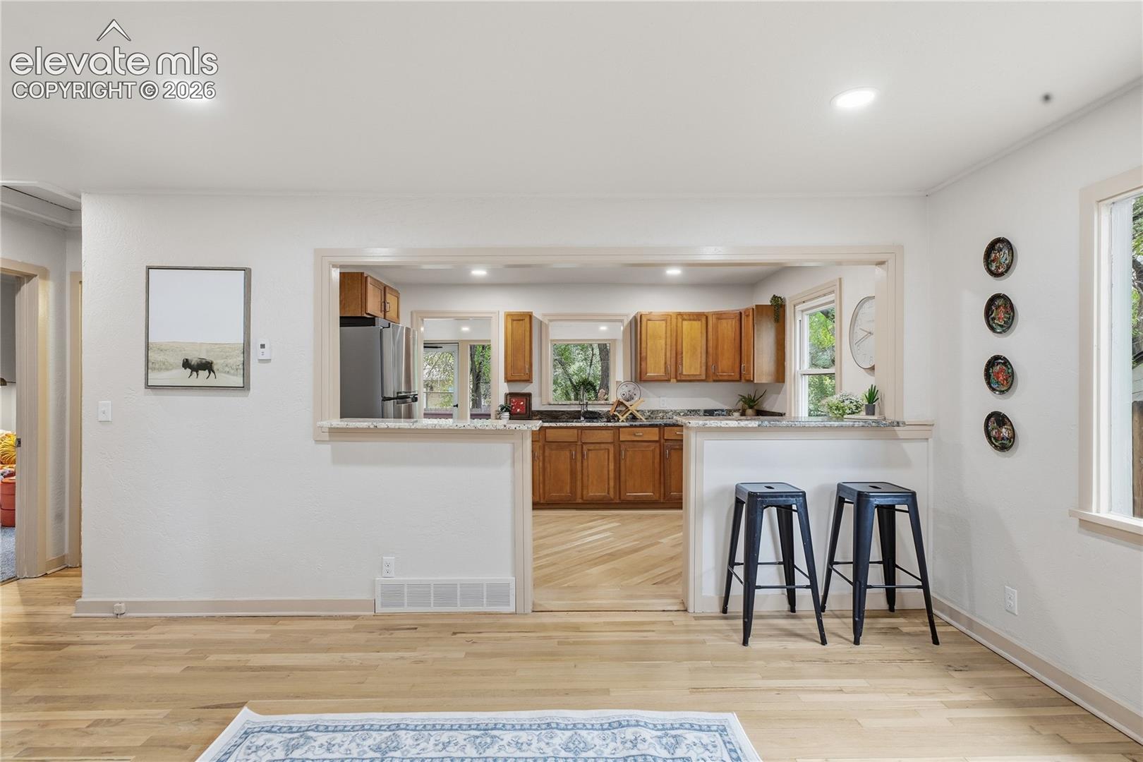 Kitchen pass-through window with a stone-surface breakfast bar, wood cabinetry, recessed lighting, and wood-finish flooring