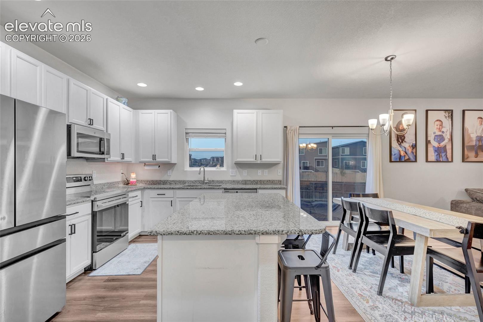 Kitchen featuring white cabinetry, stainless steel appliances, granite countertops, and wood-finish flooring
