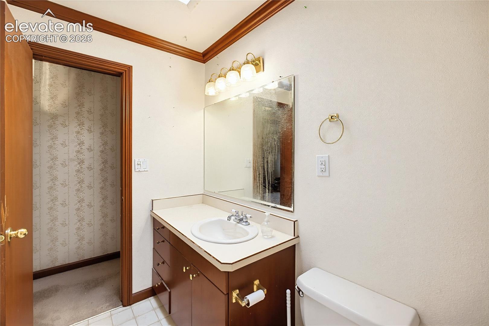 Wood-finish vanity with an integrated basin sink, mirrored wall, and brass-finish light fixture