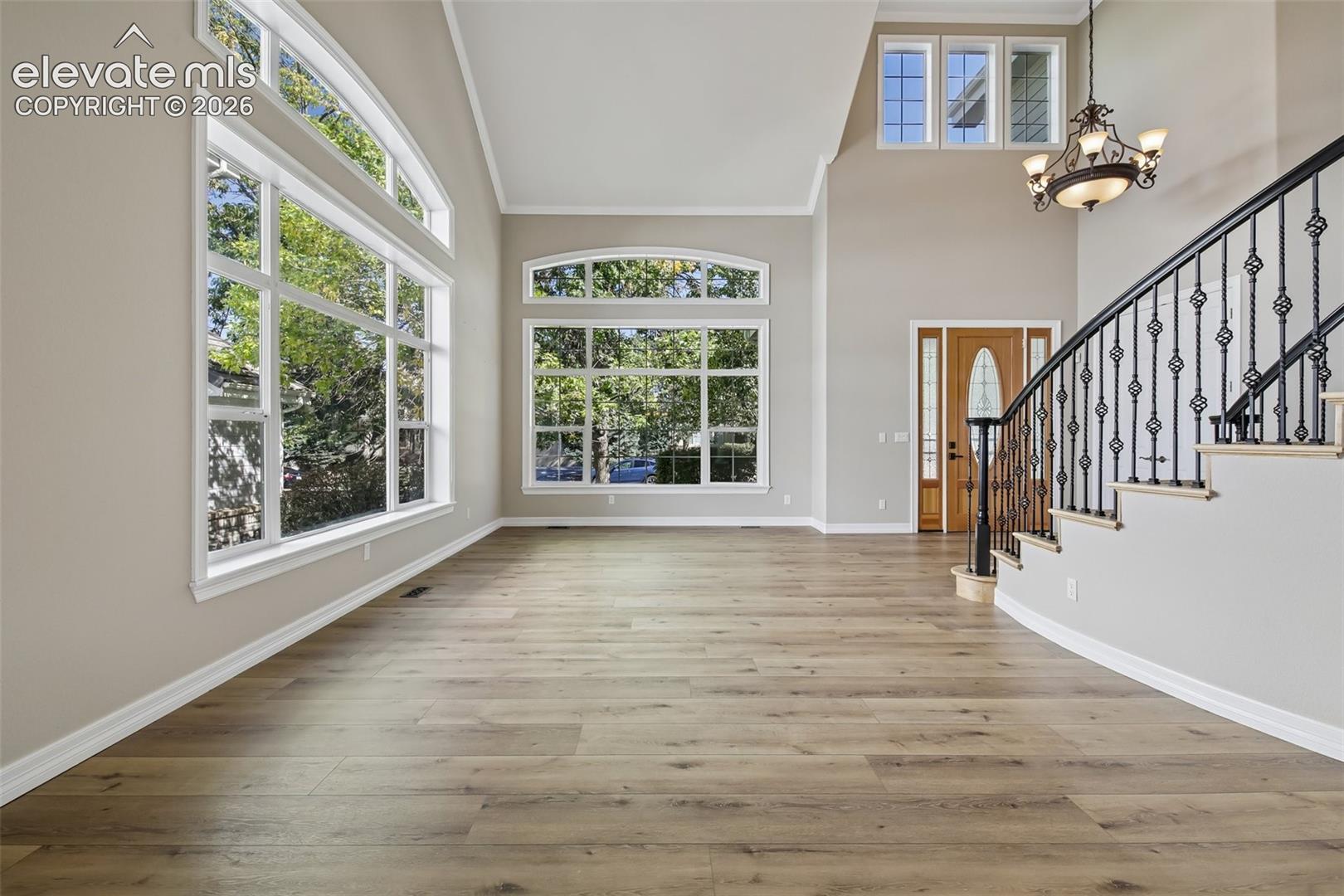 Vaulted ceiling with a decorative chandelier, expansive windows with arch detailing, wood-finish flooring, and a curved staircase with wrought iron balusters