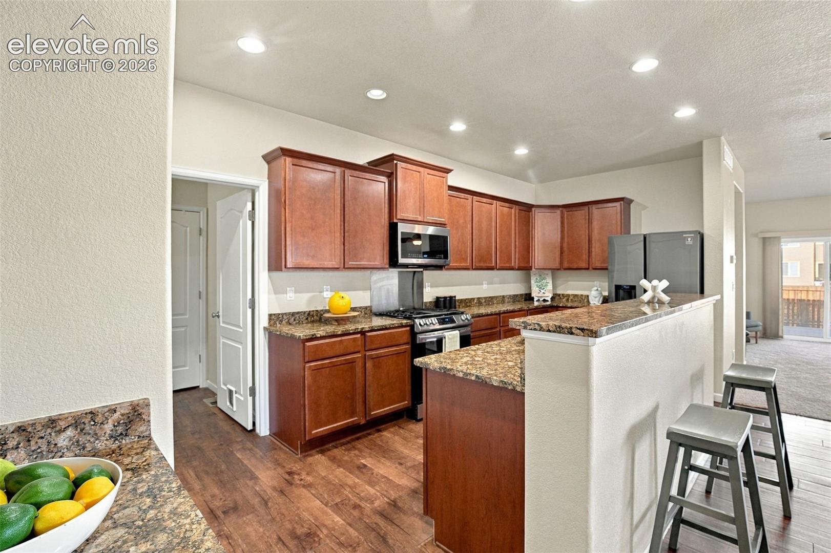 Kitchen featuring stained wood cabinetry, stone-finish countertops, recessed lighting, and wood-finish flooring