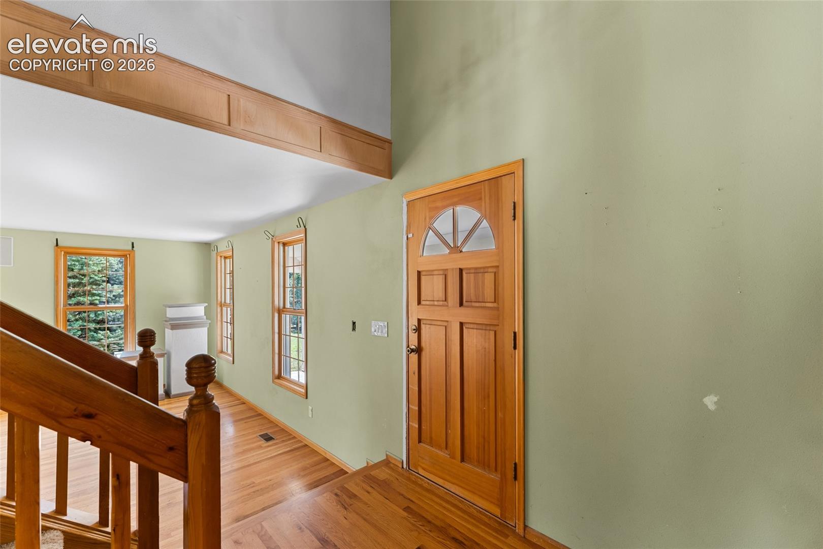 Natural wood door with an arched transom, hardwood flooring, and light green wall finish