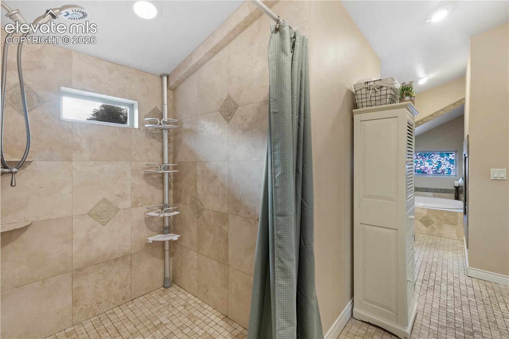 Tiled shower with handheld showerhead, corner shelf, and small rectangular window