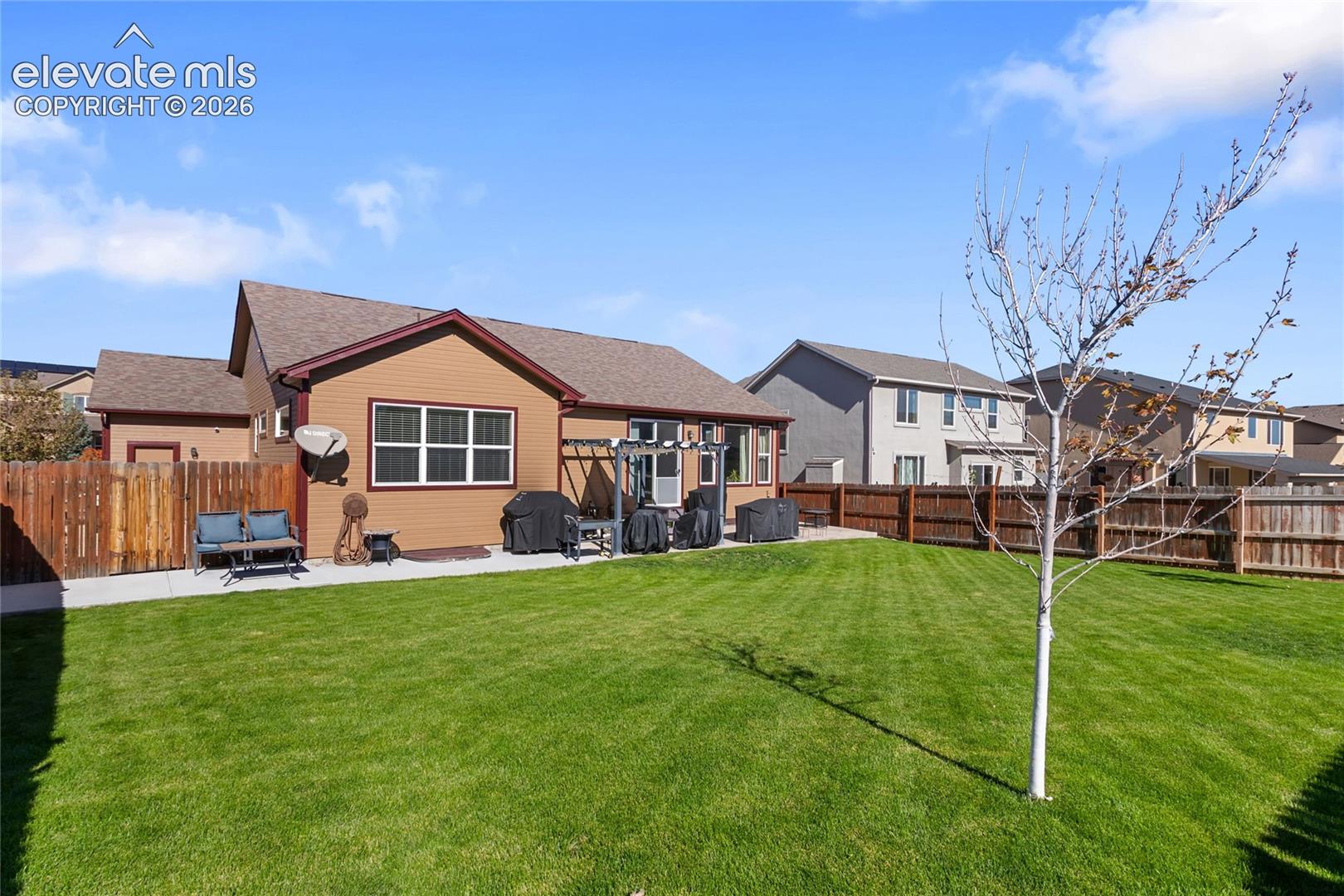 Fenced backyard featuring a manicured lawn, concrete patio, wooden pergola, and horizontal lap siding exterior