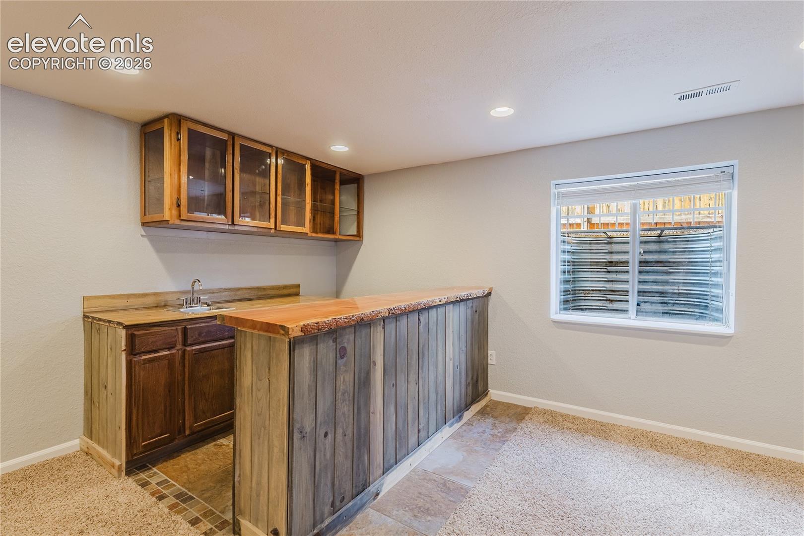 Wood-finish wet bar with built-in cabinetry, integrated sink, and recessed lighting