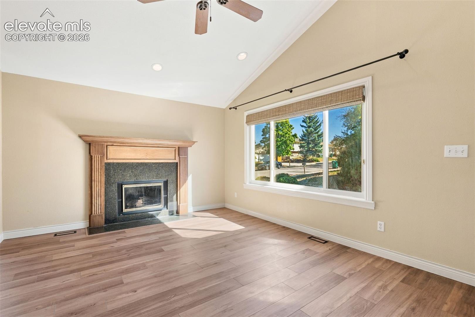 Vaulted ceiling featuring a ceiling fan, wood-finish flooring, and a fireplace with a stone surround and wood mantel