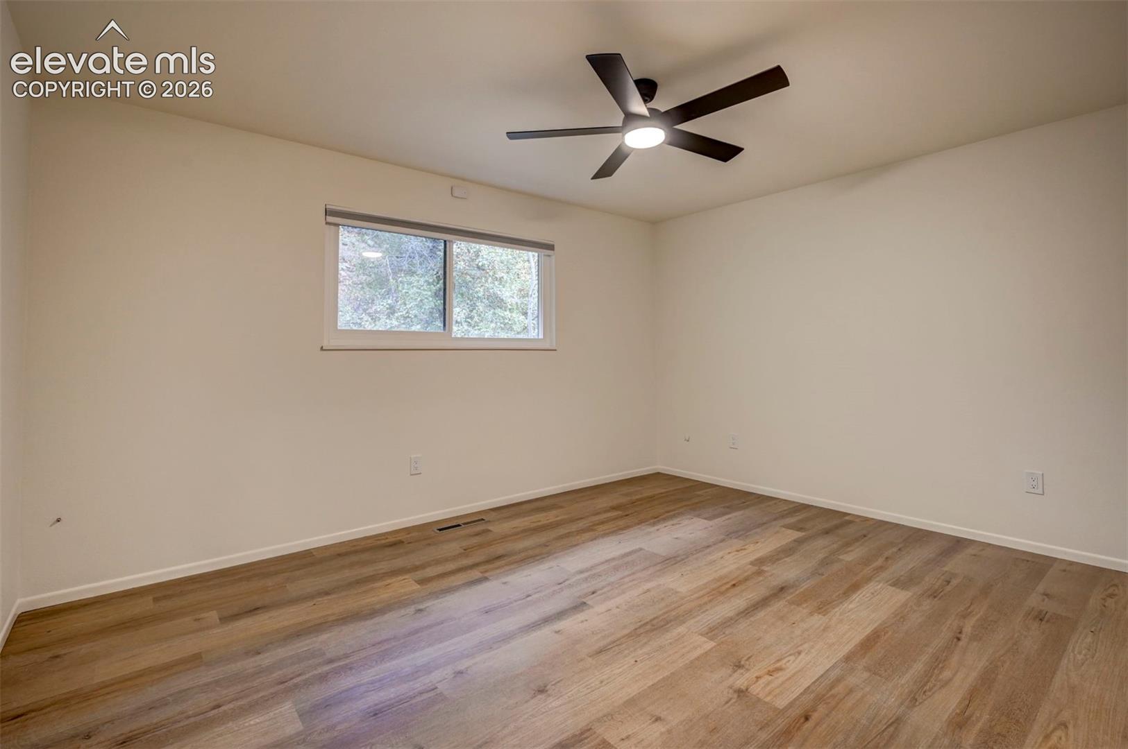 Interior space featuring wood-finish flooring, neutral wall paint, and a matte black ceiling fan with integrated lighting