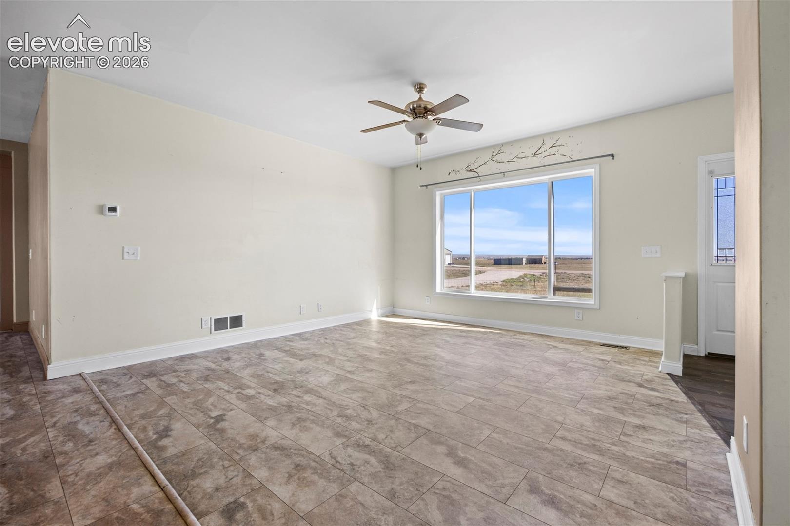 Spacious room featuring tile flooring, a multi-blade ceiling fan with integrated lighting, a large picture window, and a door with glass detailing