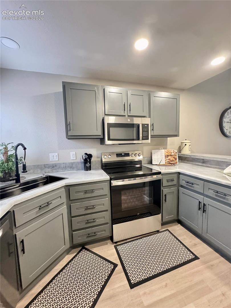 Kitchen featuring gray shaker-style cabinetry, light-toned stone-finish countertops, stainless steel appliances, and a high-arc matte black faucet