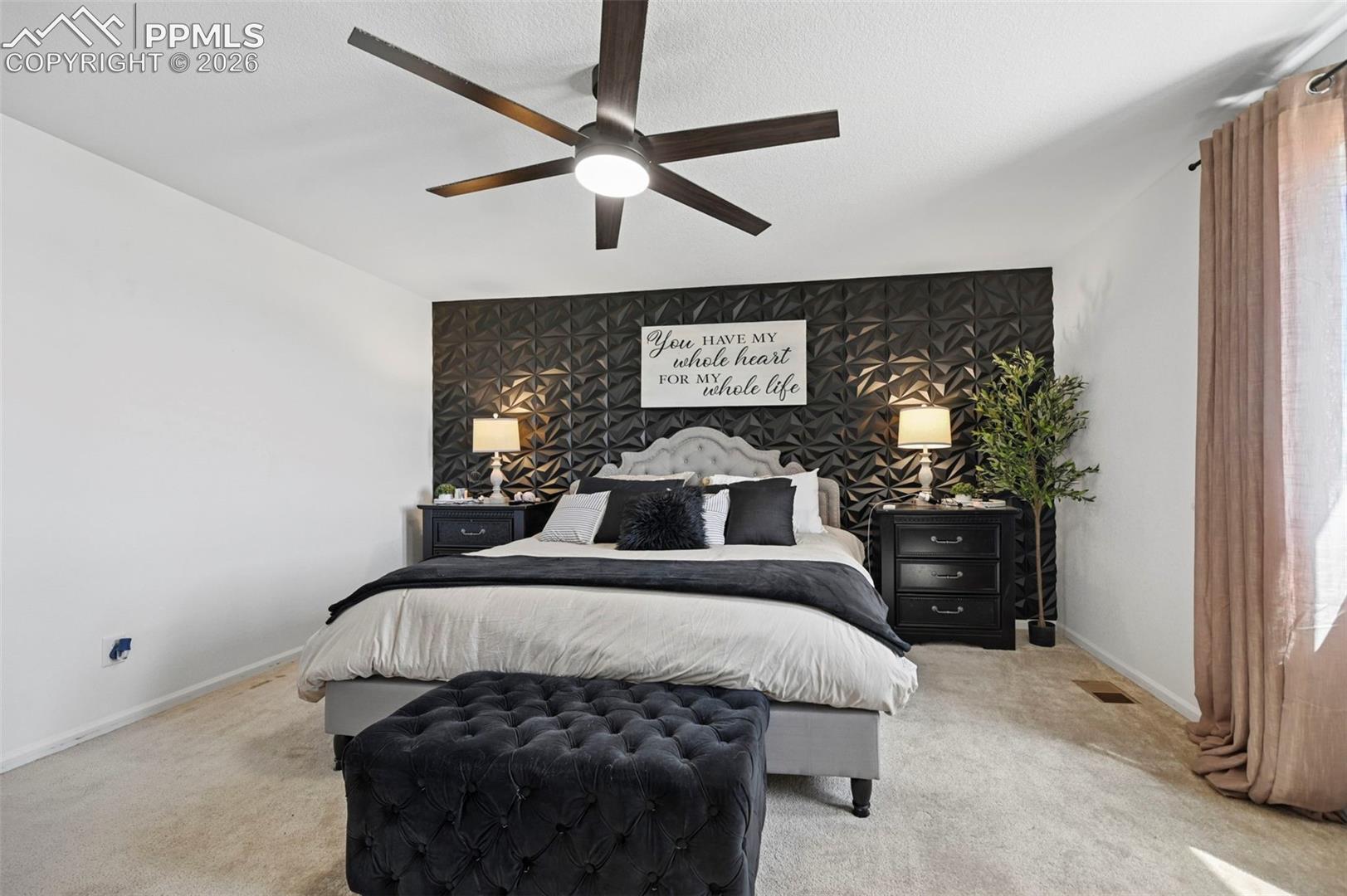 Bedroom featuring a textured accent wall, light-colored carpeting, and a ceiling fan with integrated lighting