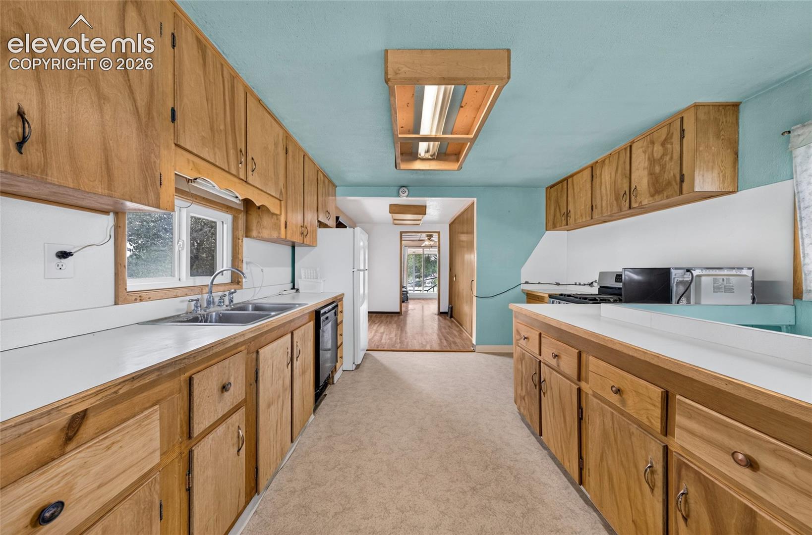 Galley kitchen featuring wood cabinetry, white countertops, a double basin sink, and a built-in dishwasher