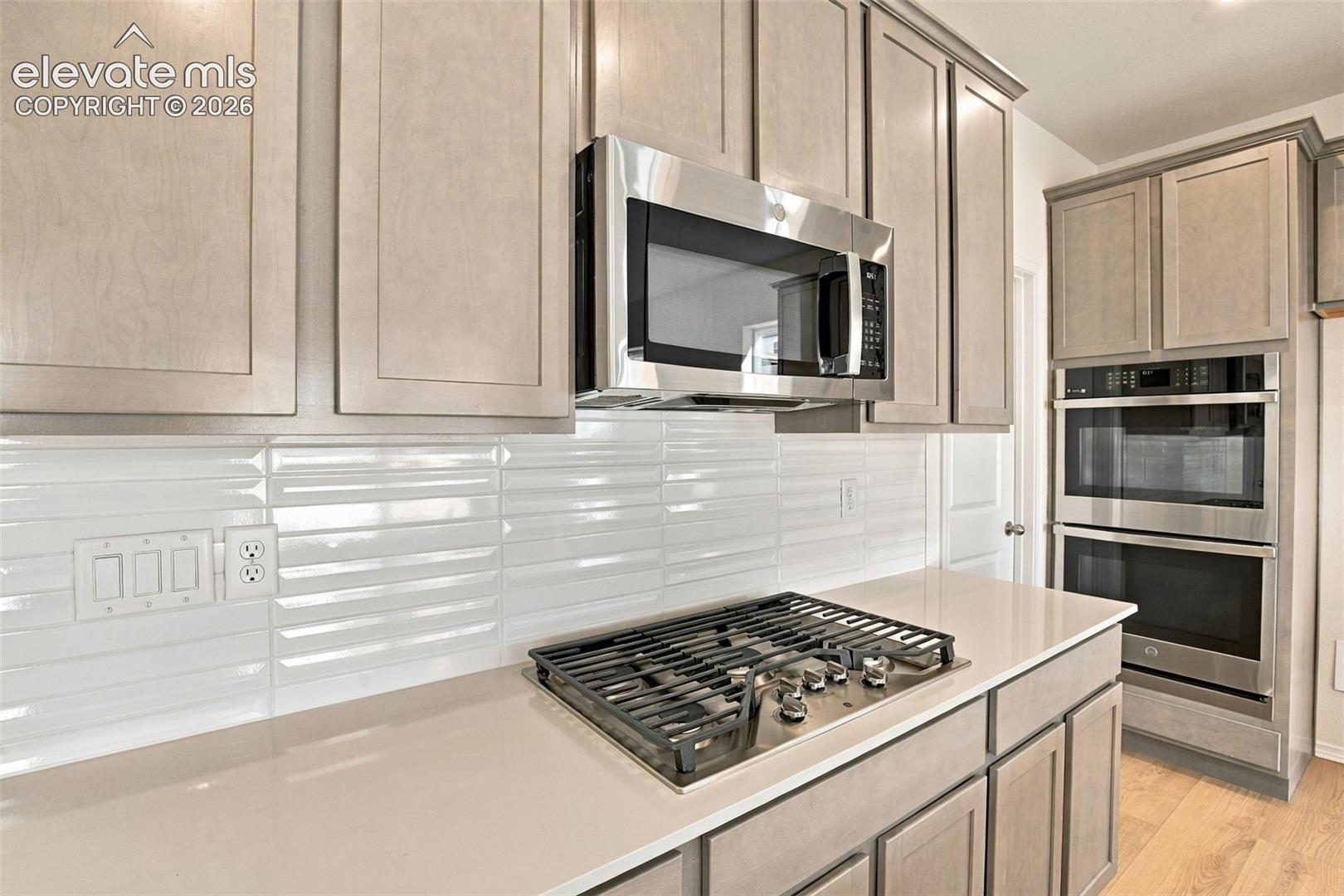 Custom cabinetry with a neutral finish, stone-surface countertops, textured white tile backsplash, integrated stainless steel appliances, and gas cooktop