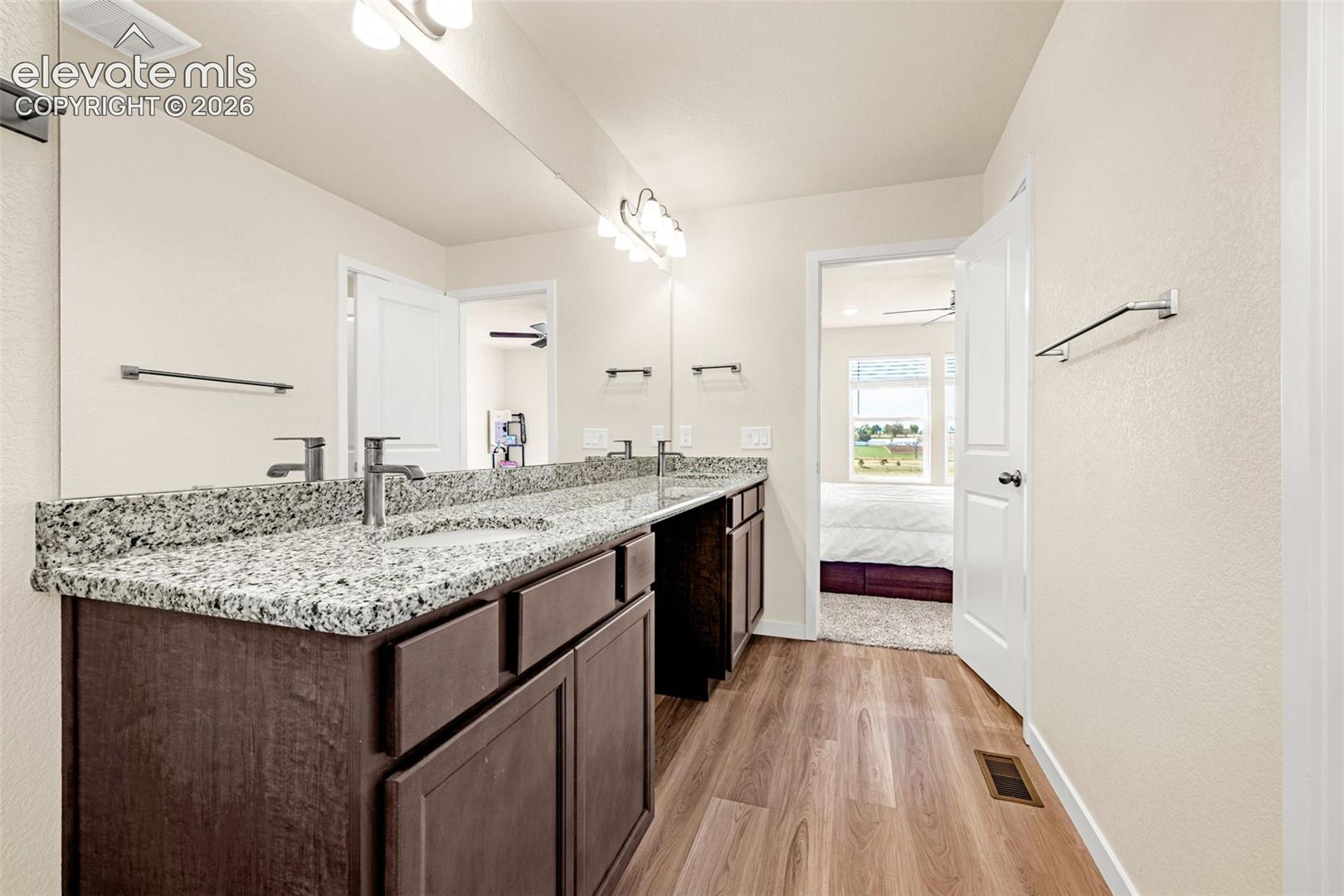 Double vanity with granite countertop, dual sinks, wood-finish flooring, and recessed lighting