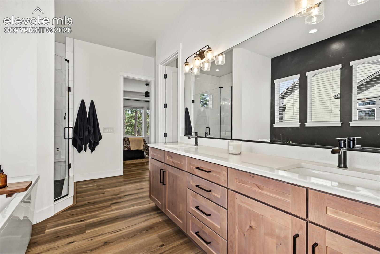 Beautifully appointed primary bathroom featuring an expansive dual-sink vanity, warm cabinetry, elegant lighting, and modern finishes.