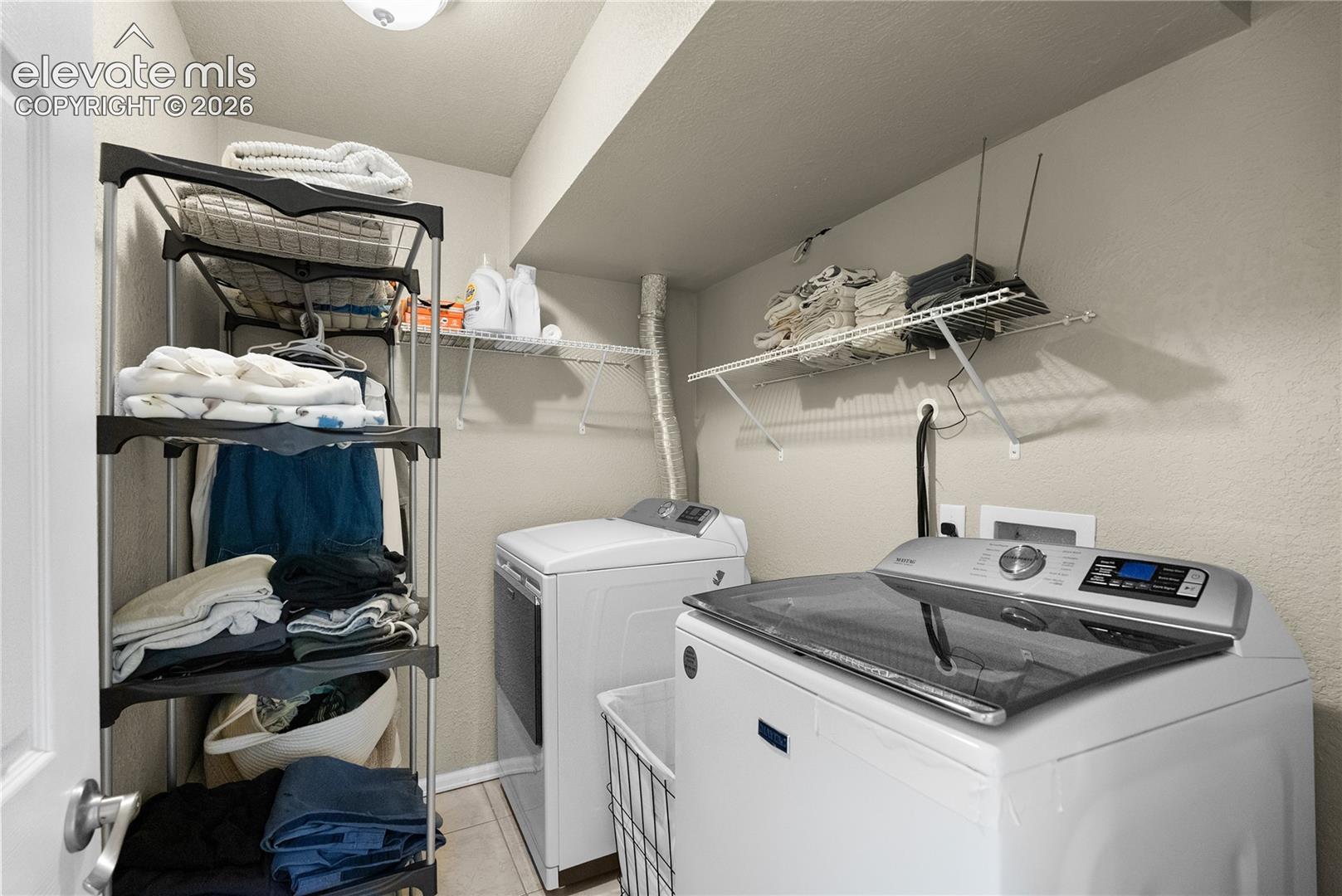Laundry area with tile flooring and a wall-mounted wire shelf