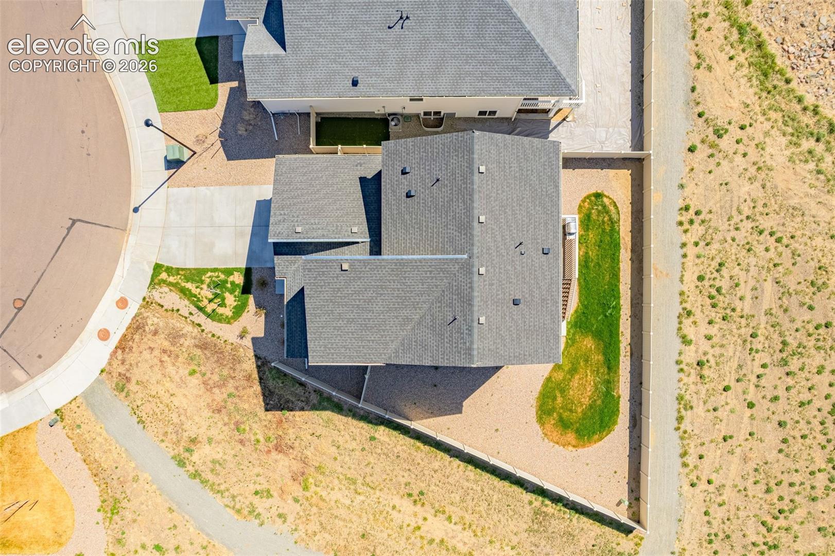 Pitched roofline, concrete driveway, paved sidewalk, surrounding natural landscaping, and a manicured lawn area