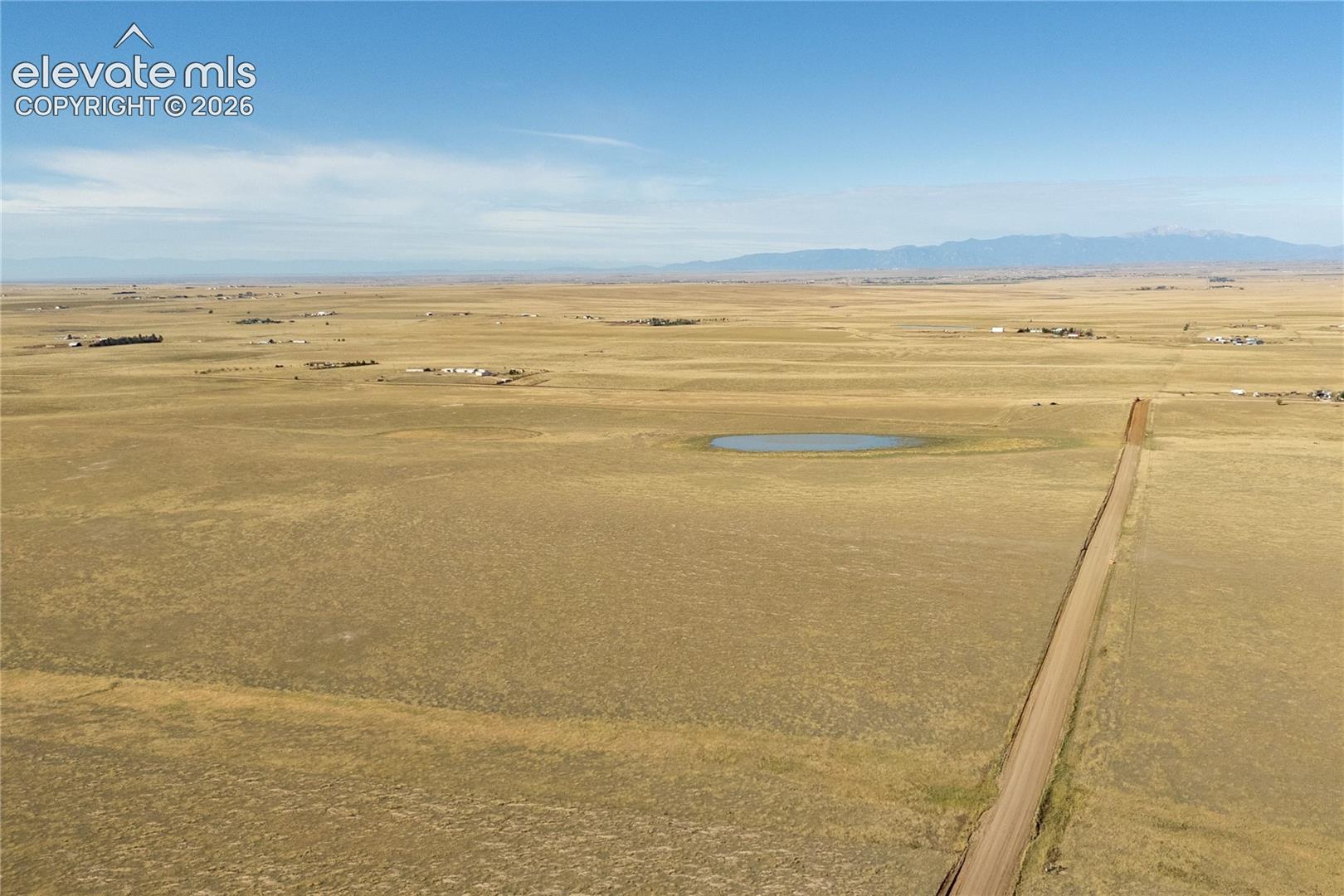 Expansive acreage featuring native grasslands, a natural water pond, a gravel access road, and mountain backdrop
