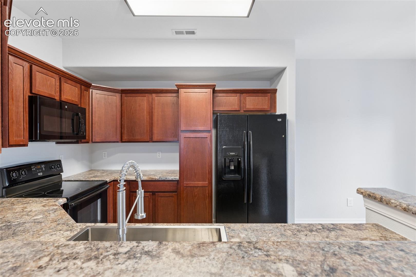 Kitchen featuring wood-tone cabinetry, stone-finish countertops, stainless steel undermount sink with a gooseneck faucet, and black built-in appliances