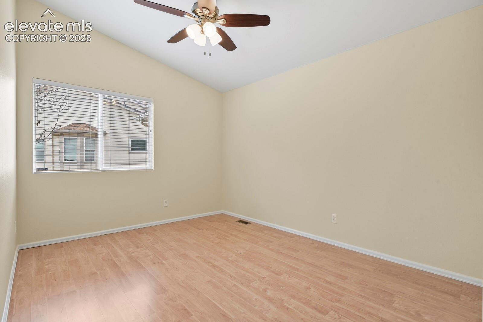 Spacious room featuring vaulted ceilings, wood-finish flooring, a contemporary ceiling fan with integrated lighting, and a large window with horizontal blinds