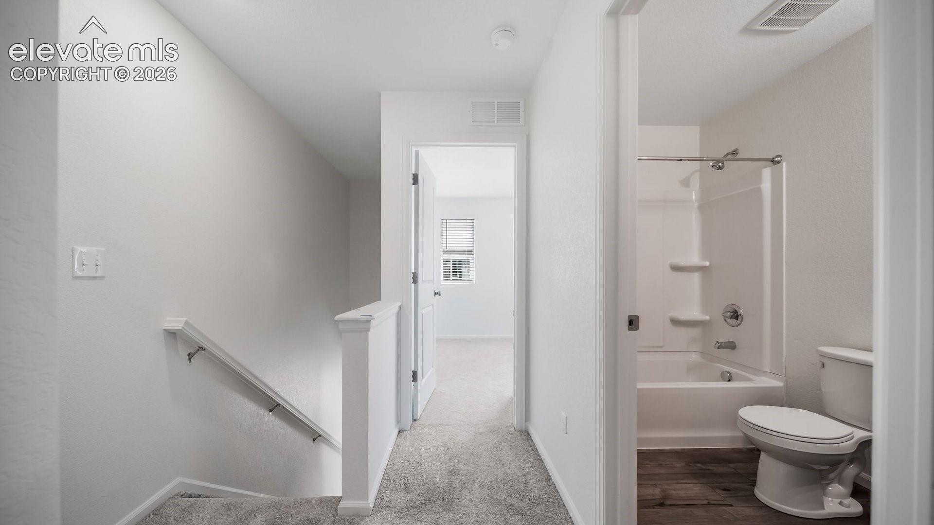 Bathroom featuring a shower and tub combination with integrated shelving, a toilet, and wood-finish flooring
*photos of a model home*