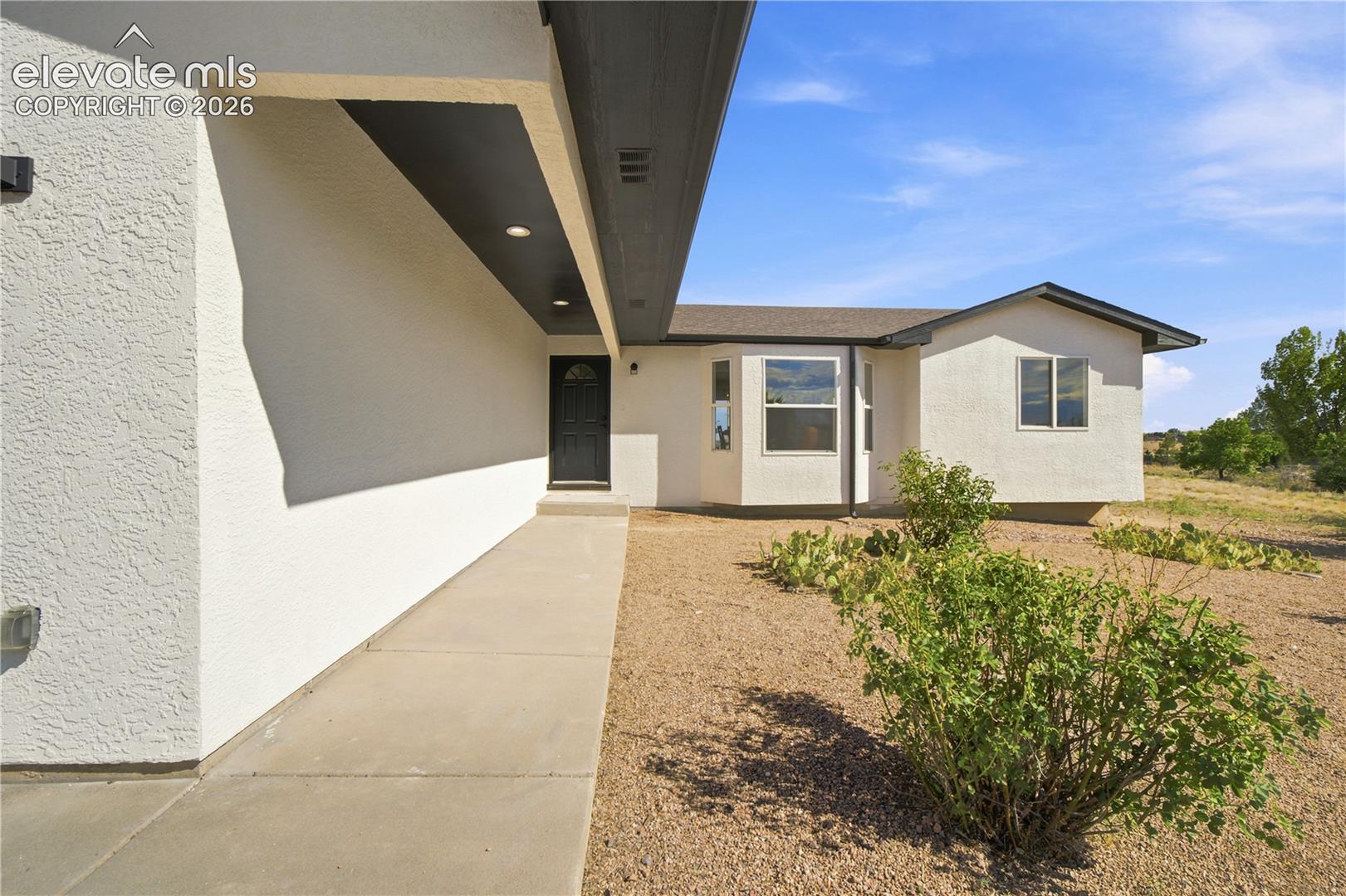 Contemporary stucco exterior with a covered entry, recessed lighting, and a dark paneled entry door