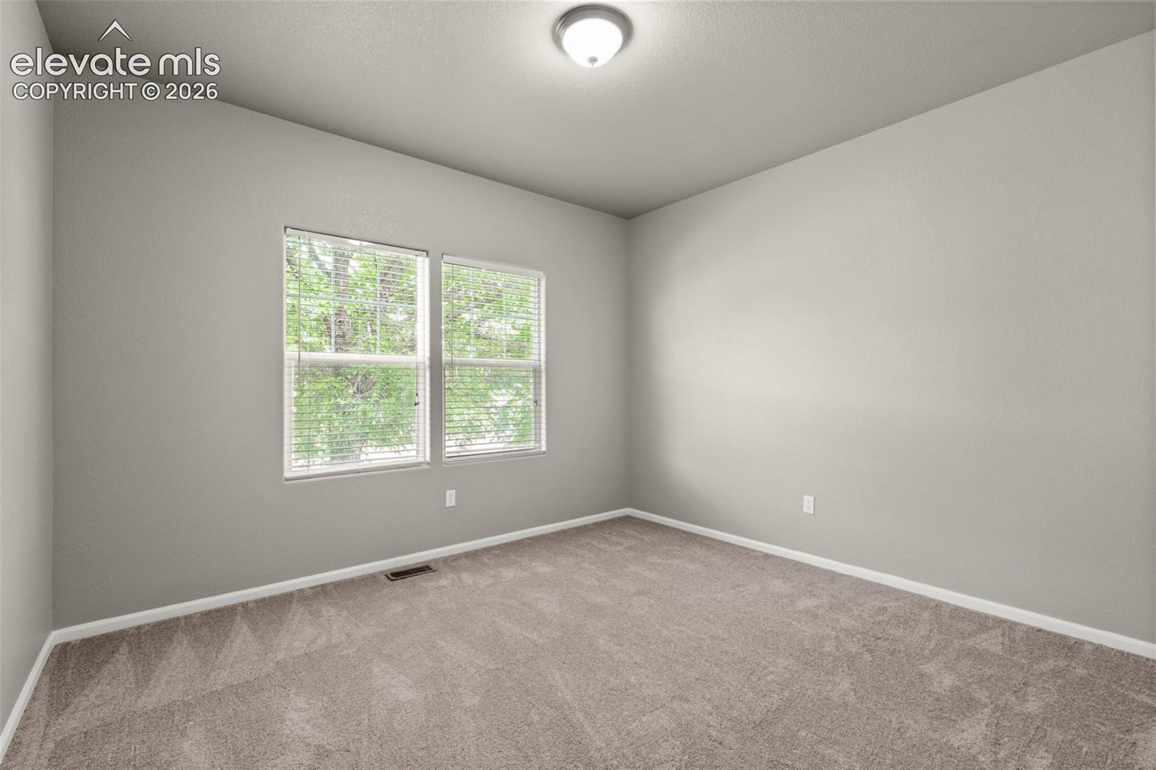 Neutral interior room featuring neutral wall paint, plush carpeting, dual-pane windows with integrated blinds, and a flush-mount ceiling light fixture