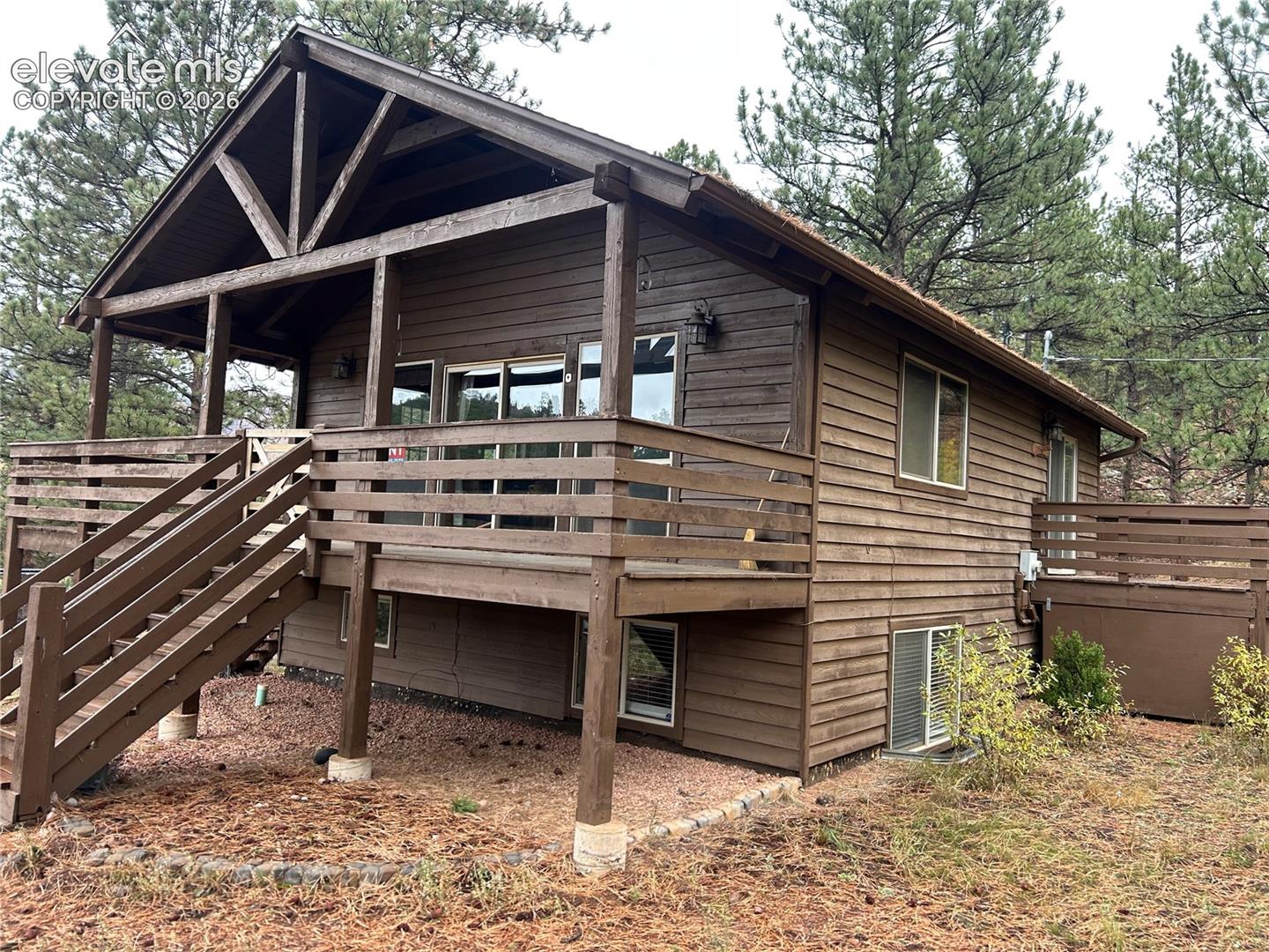 Wood-sided home exterior featuring a covered front porch, structural timber framing, a raised deck with wood railings, and sliding glass entry doors