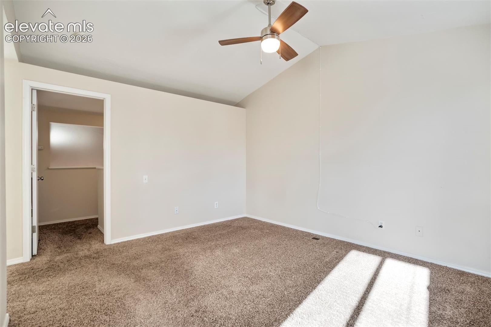 Interior space featuring vaulted ceilings, neutral wall tones, textured carpeting, and a brushed nickel ceiling fan with integrated lighting