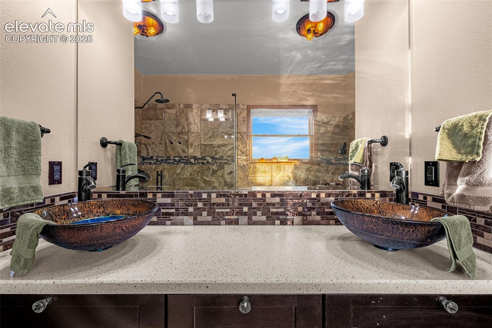 Dual vessel sinks with bronze-finish fixtures, a large mirror, and a tiled backsplash