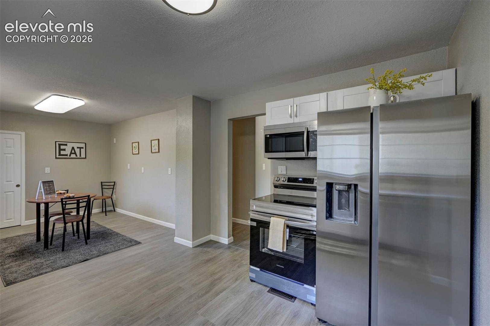 Kitchen featuring white shaker-style cabinetry, stainless steel appliances, a built-in over-the-range microwave, and wood-finish flooring
