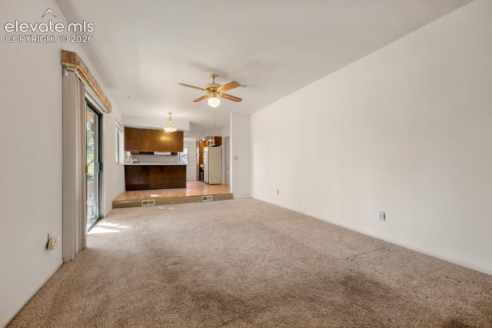 Interior space featuring neutral carpeting, a dual-level floor plan, wood-finish cabinetry, and a ceiling fan